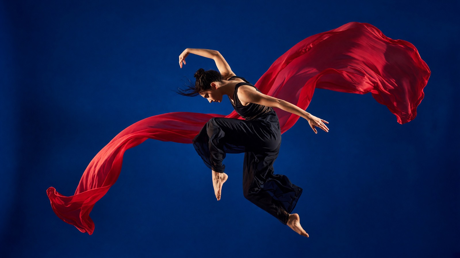 Contemporary dancer suspended with flowing crimson fabric on cobalt blue generated with Grok Imagine Image V2.0